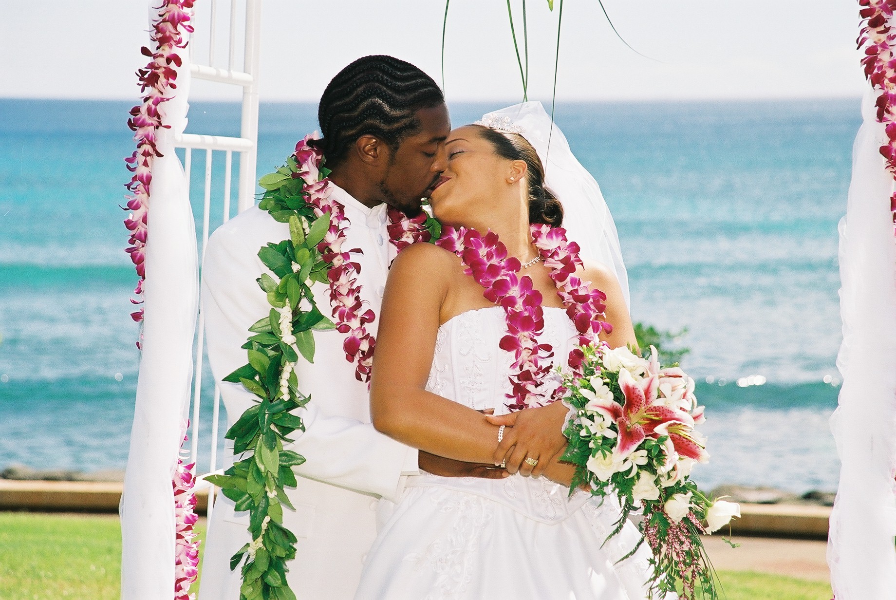 Couple kissing with orchid leis under white drapes by the ocean